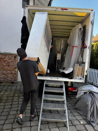 Umzugsteam trägt einen verpackten Schrank aus dem LKW